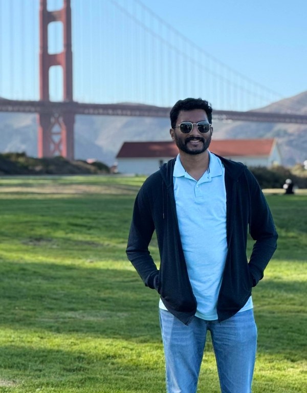 Abhilash John Philip in a light-blue polo and dark hoodie, standing on a lawn near the Golden Gate Bridge